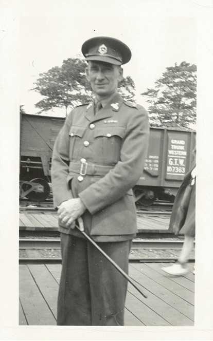 Black and white photograph. Archie poses and smiles for the camera in his uniform, in front of a train car.